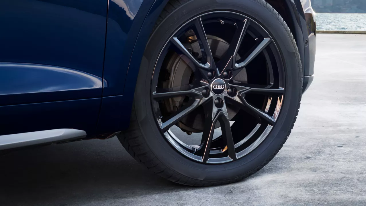 A close up of the front right wheel of a navy blue Audi vehicle, Audi logo visible on the wheel