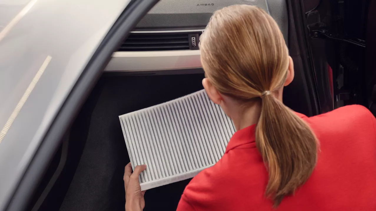 An Audi mechanic, holding a car part and leaning into the front interior of an Audi vehicle