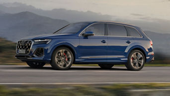 A blue Audi SUV in motion on a road with a mountainous backdrop.