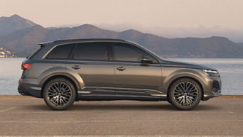 A grey SUV parked by the sea with mountains in the background.