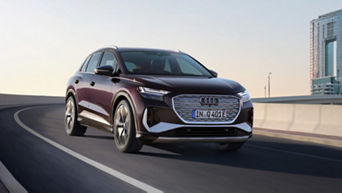 A maroon Audi electric vehicle driving on a highway with city buildings in the background.