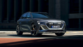 A black Audi electric vehicle driving on a sunny city street