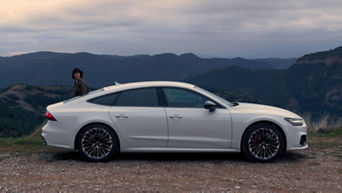 A silver Audi vehicle parked on a hilltop with a scenic mountain backdrop