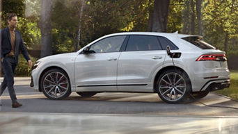 A silver Audi vehicle parked outdoors near trees, under sunlight