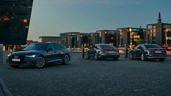 Three Audi vehicles parked together in the evening, modern buildings lit up in the background