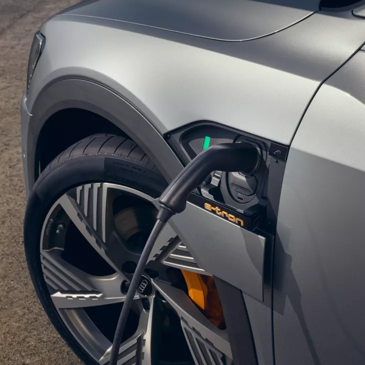 An Audi electric vehicle being charged, with the charging cable connected to the front-side port.