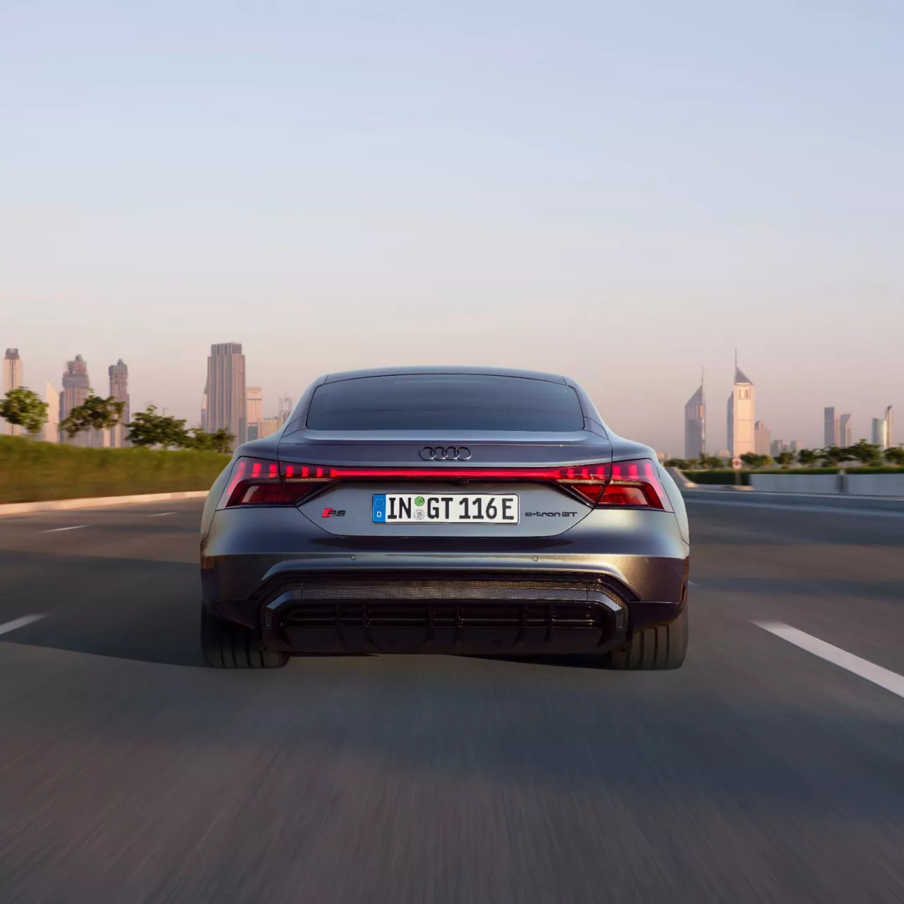 An Audi e-tron GT viewed from the rear on a road driving towards a cityscape in the distance