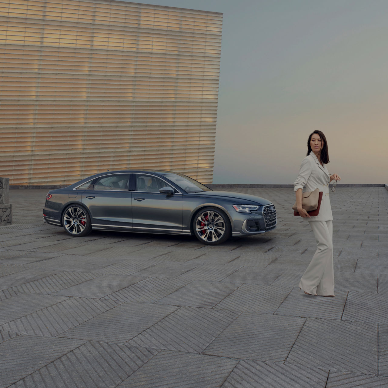 A sedan parked on a rooftop with a geometric patterned floor, near a textured wall, at dusk.