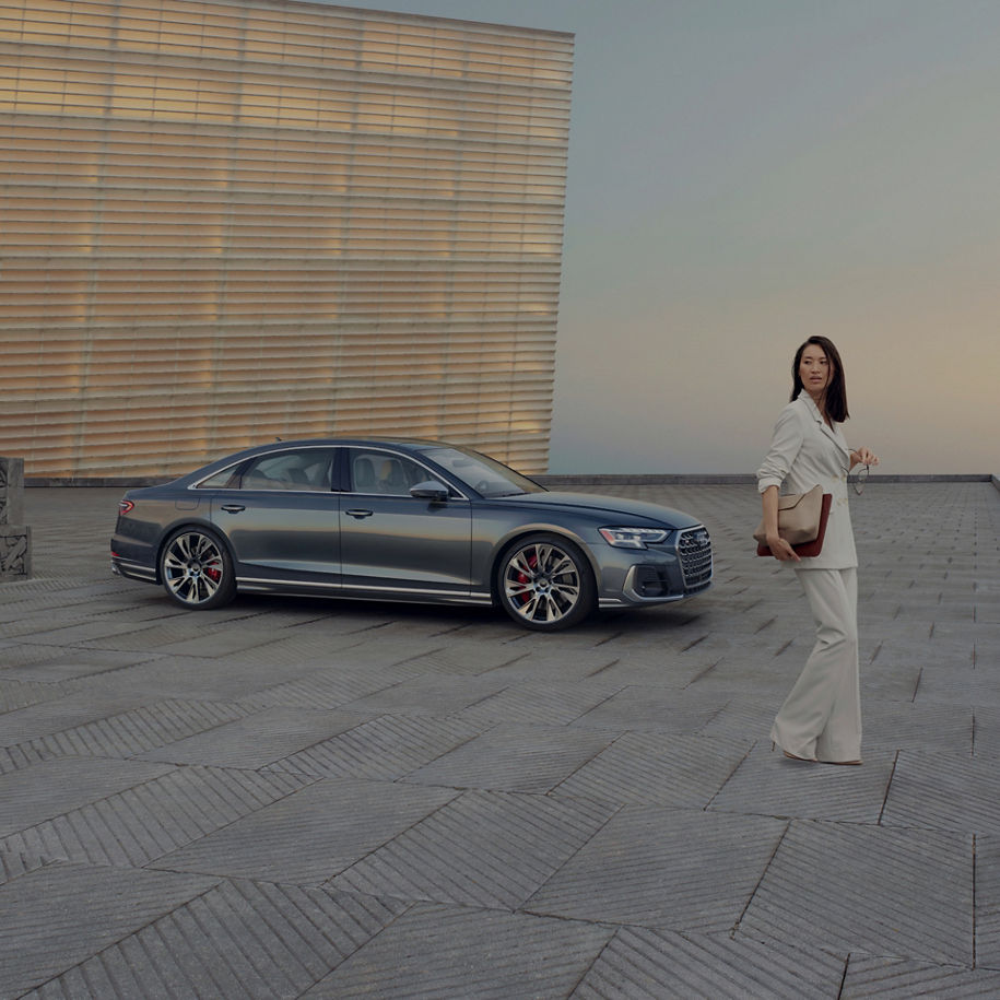 A sedan parked on a rooftop with a geometric patterned floor, near a textured wall, at dusk.