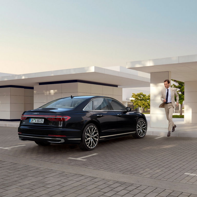 A black Audi parked outside a modern building with a person walking nearby.