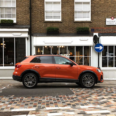 Side view of pulse orange Audi Q3 outside a café on a high street.