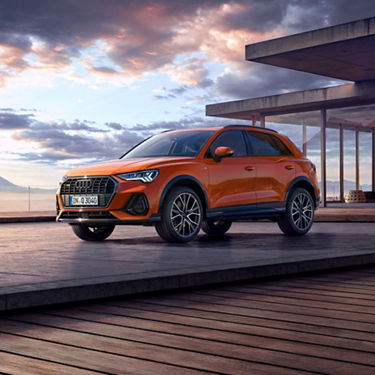 Angled front view of an Audi Q3 on a patio outside a beach house with an open cloudy sky in the background.