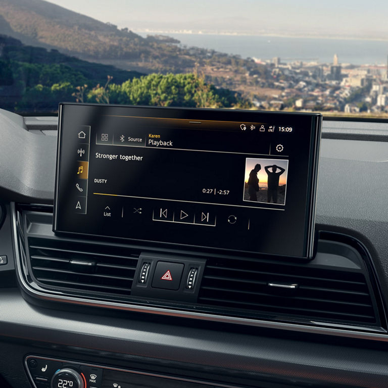 Car dashboard with infotainment screen displaying a music player interface and navigation map.