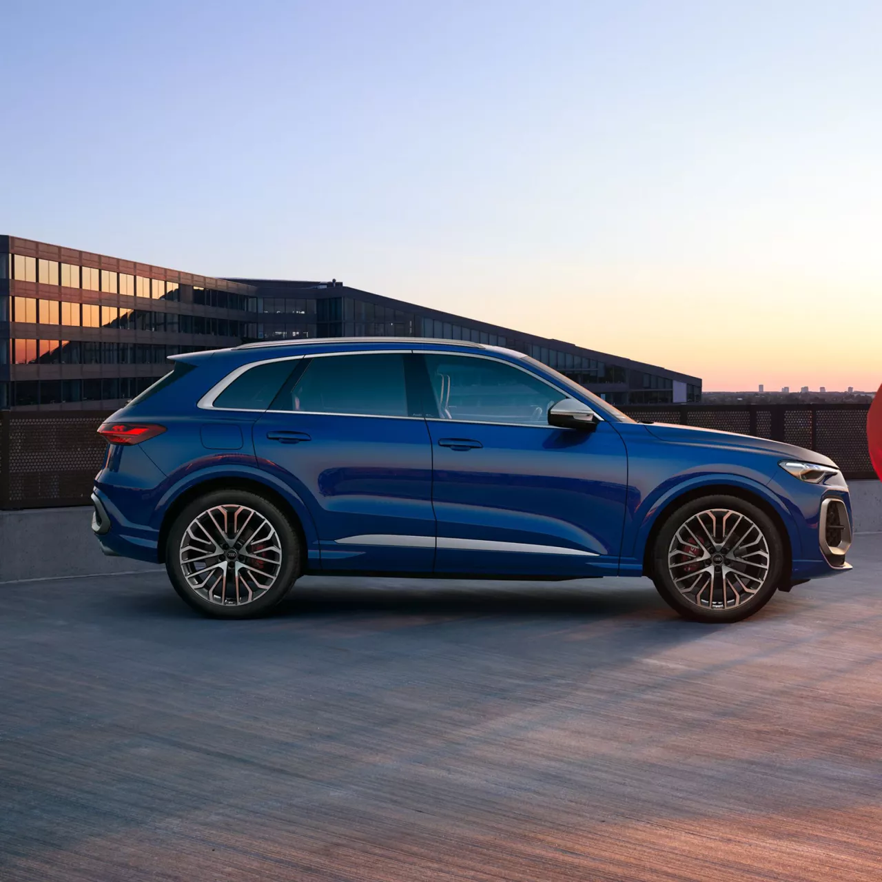 Blue SUV parked on rooftop at dusk with modern buildings in the background.