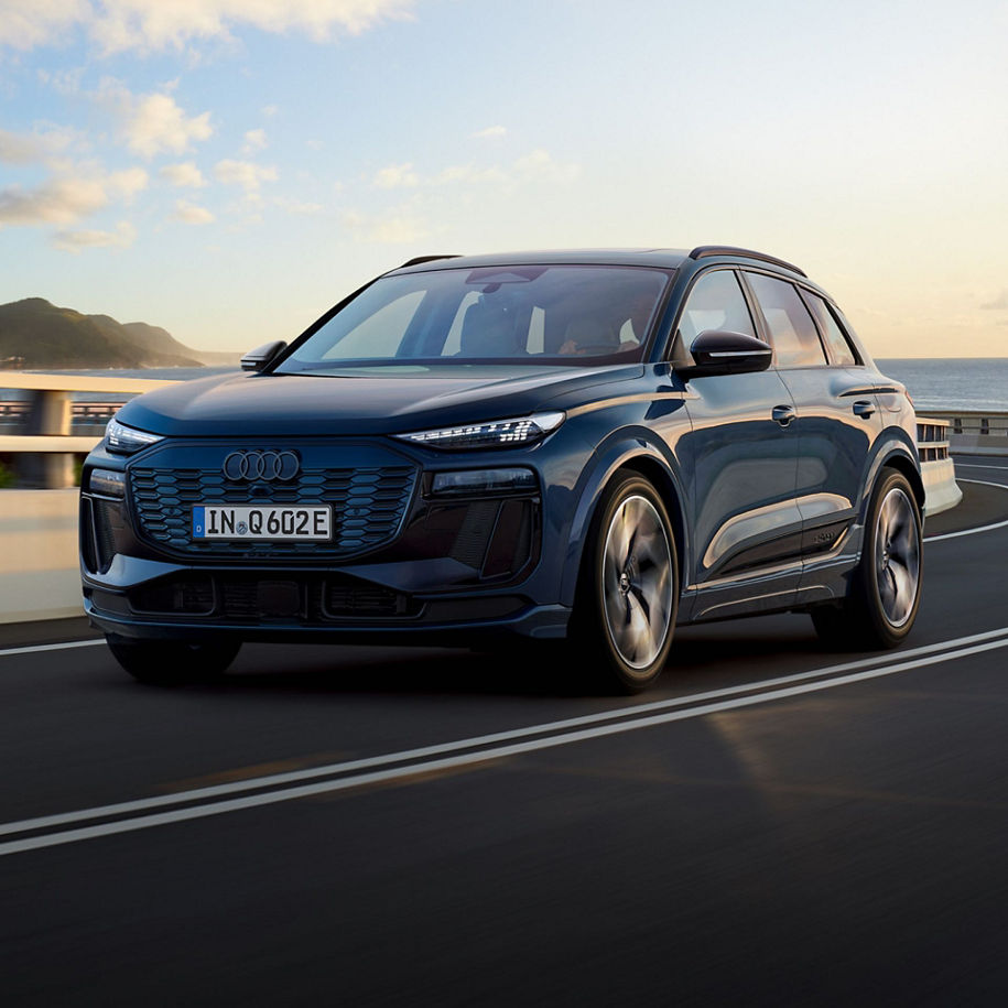 A blue Audi electric SUV driving on a coastal road at sunset.