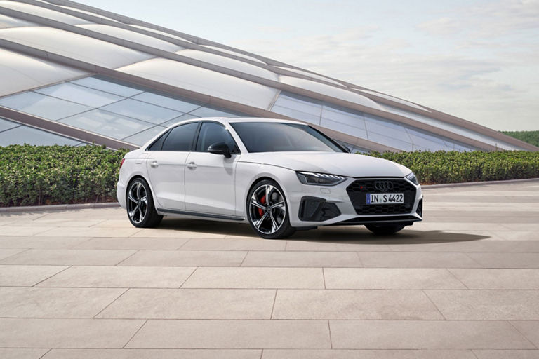 A white Audi sedan parked outdoors with modern architecture in the background.