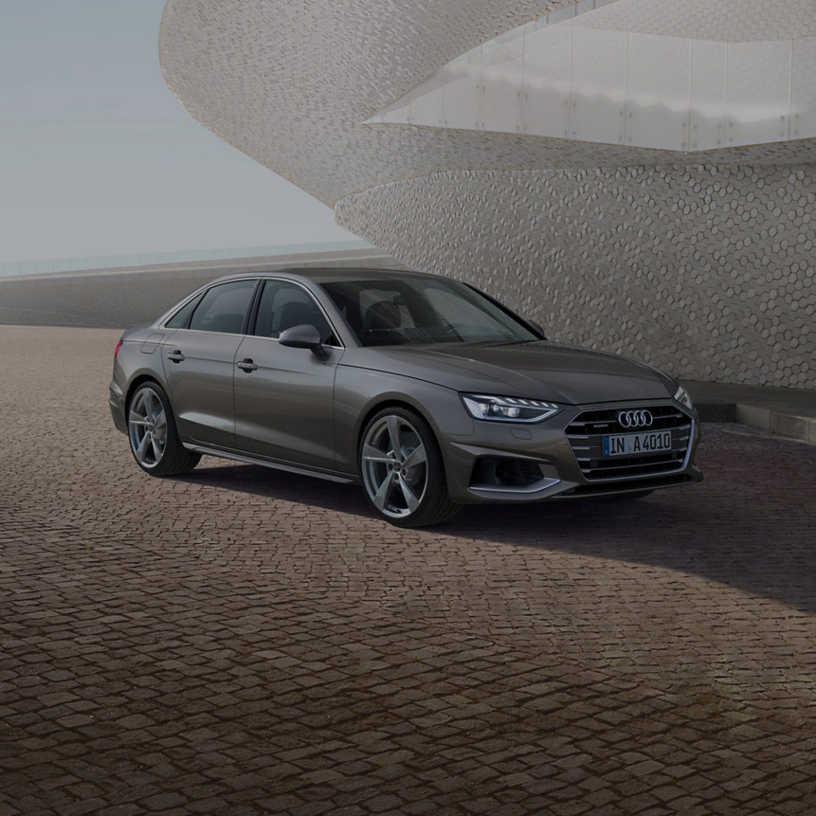 A grey Audi sedan parked near a unique textured building under a clear sky.