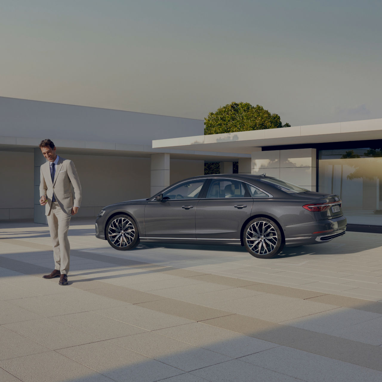 man in white suit standing infront of dark grey Audi A8