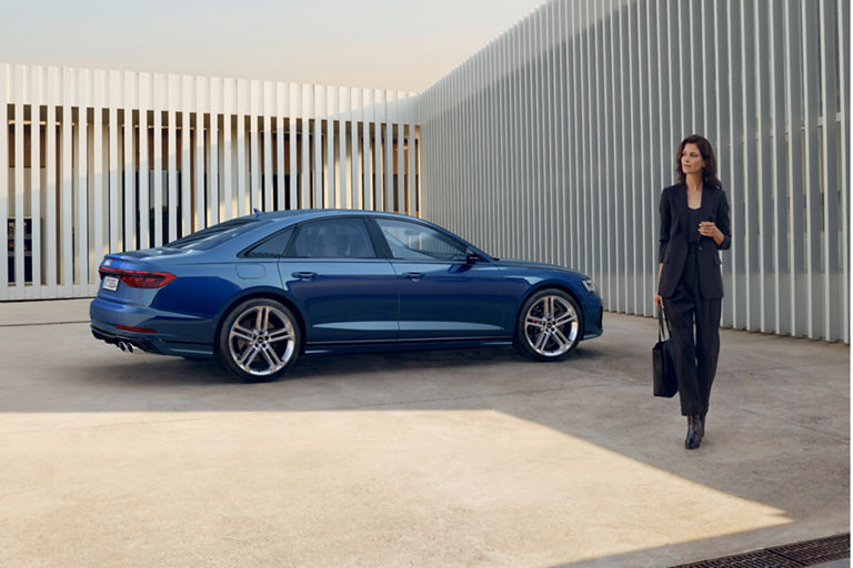 portrait image lady standing left of blue Audi A8 S8