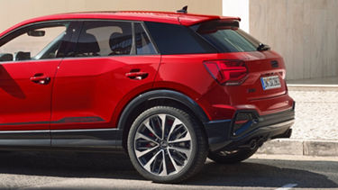 Red SUV parked, rear three-quarter view, on a cobblestone street.