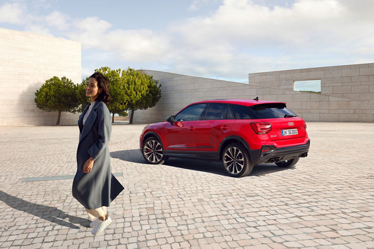 A red Audi SUV parked in a plaza with trees and modern architecture in the background.