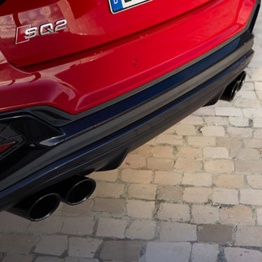 Red car's rear view featuring emblem, bumper, and dual exhausts on a cobblestone surface.