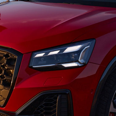 Close-up of a red car's LED headlight and grille detail. 