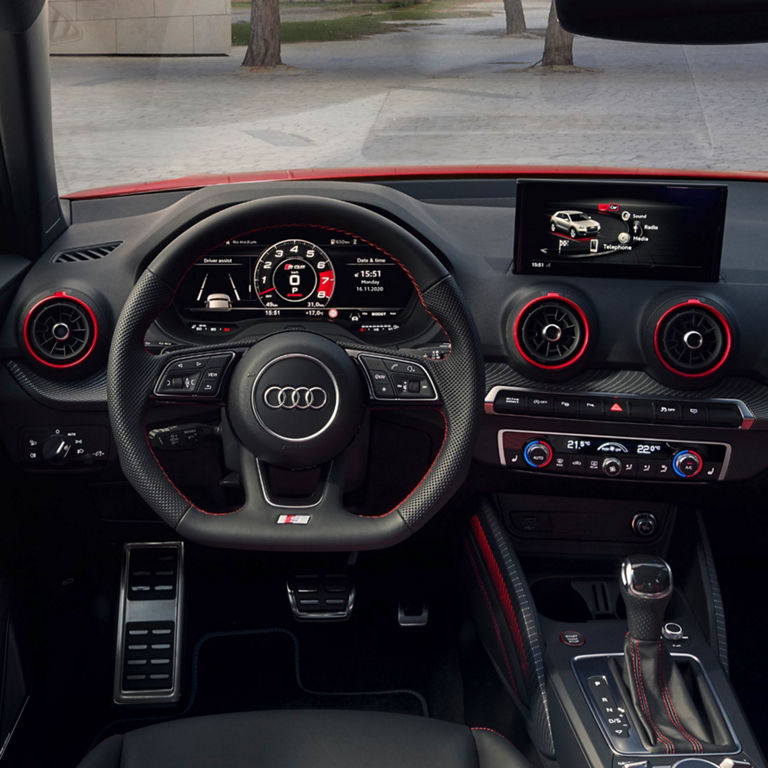 Interior of an Audi vehicle showcasing the steering wheel and dashboard with red accents.