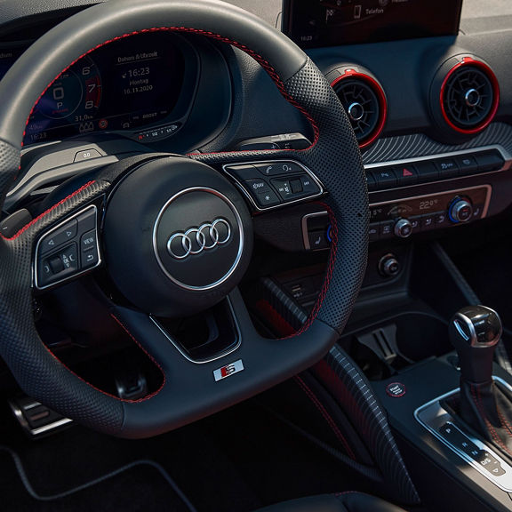 Interior view of an Audi vehicle focusing on the steering wheel and center console with red accents.