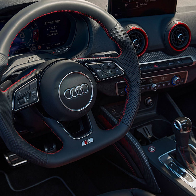 Interior view of an Audi vehicle focusing on the steering wheel and center console with red accents.