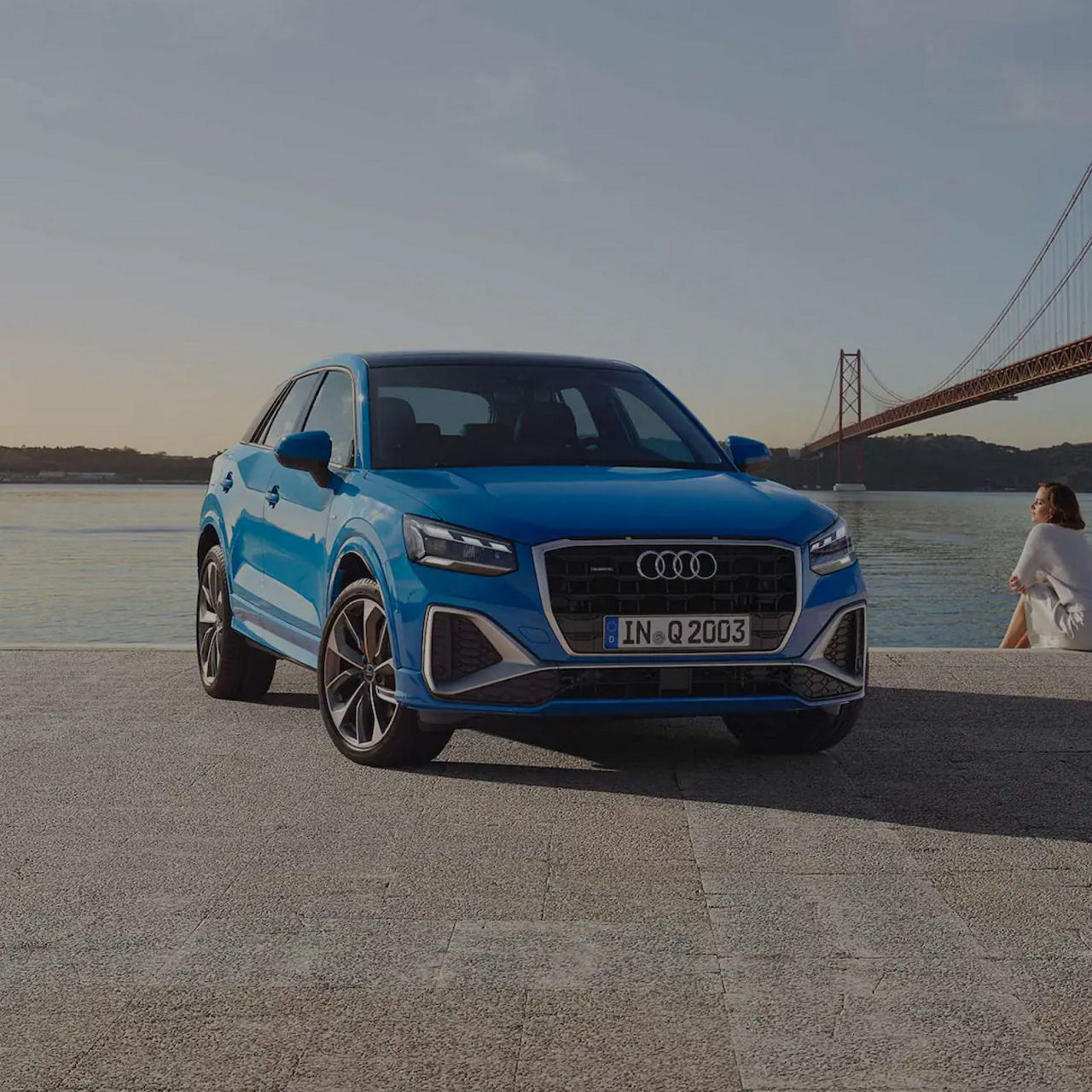 Blue Audi SUV parked by a river with a bridge in the background.