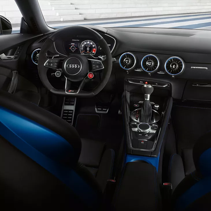 View of driver seat, controls and display console of blue Audi TT RS Coupé.