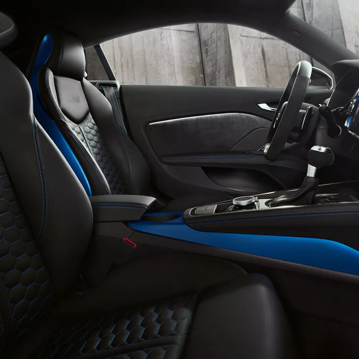 Interior view of driver and passenger seats of a blue Audi TT RS Coupe.