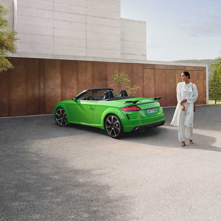 Lady in a white outfit walking away from a green parked Audi TT RS Roadster.