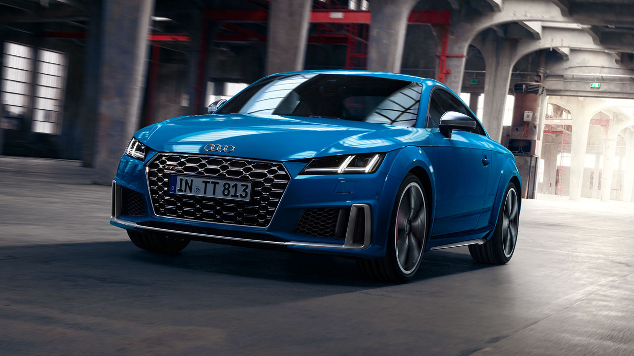 Angled front view of blue Audi TTS inside a car park.