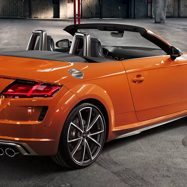 Back and side angled view of orange Audi TTS Roadster parked in a garage.