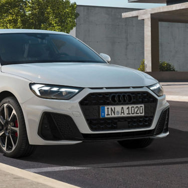 A white Audi A1 Sportback car parked outdoors with a modern building in the background.