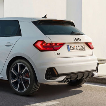 Rear view of a white Audi A1 Sportback parked next to a wall, in sunlight.