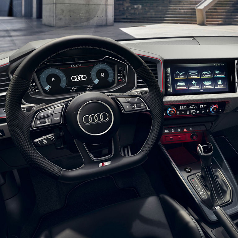 Interior view of an Audi A1 Sportback car, featuring a modern dashboard with digital displays, a multi-functional steering wheel, and a sleek gear shifter. The design showcases high-quality materials and advanced technology, emphasizing luxury and performance.