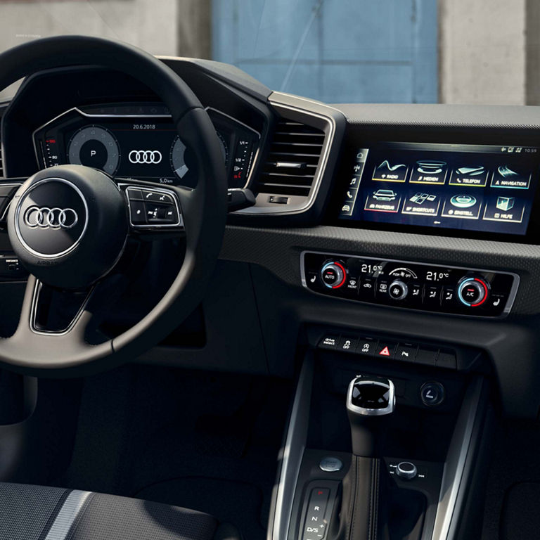 Interior of an Audi car with steering wheel, touchscreen dashboard, and gearshift.