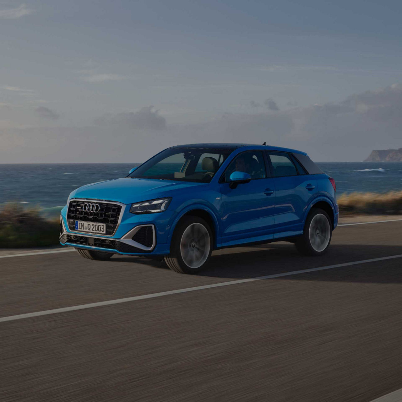 A blue Audi Q2 car driving along a coastal road.