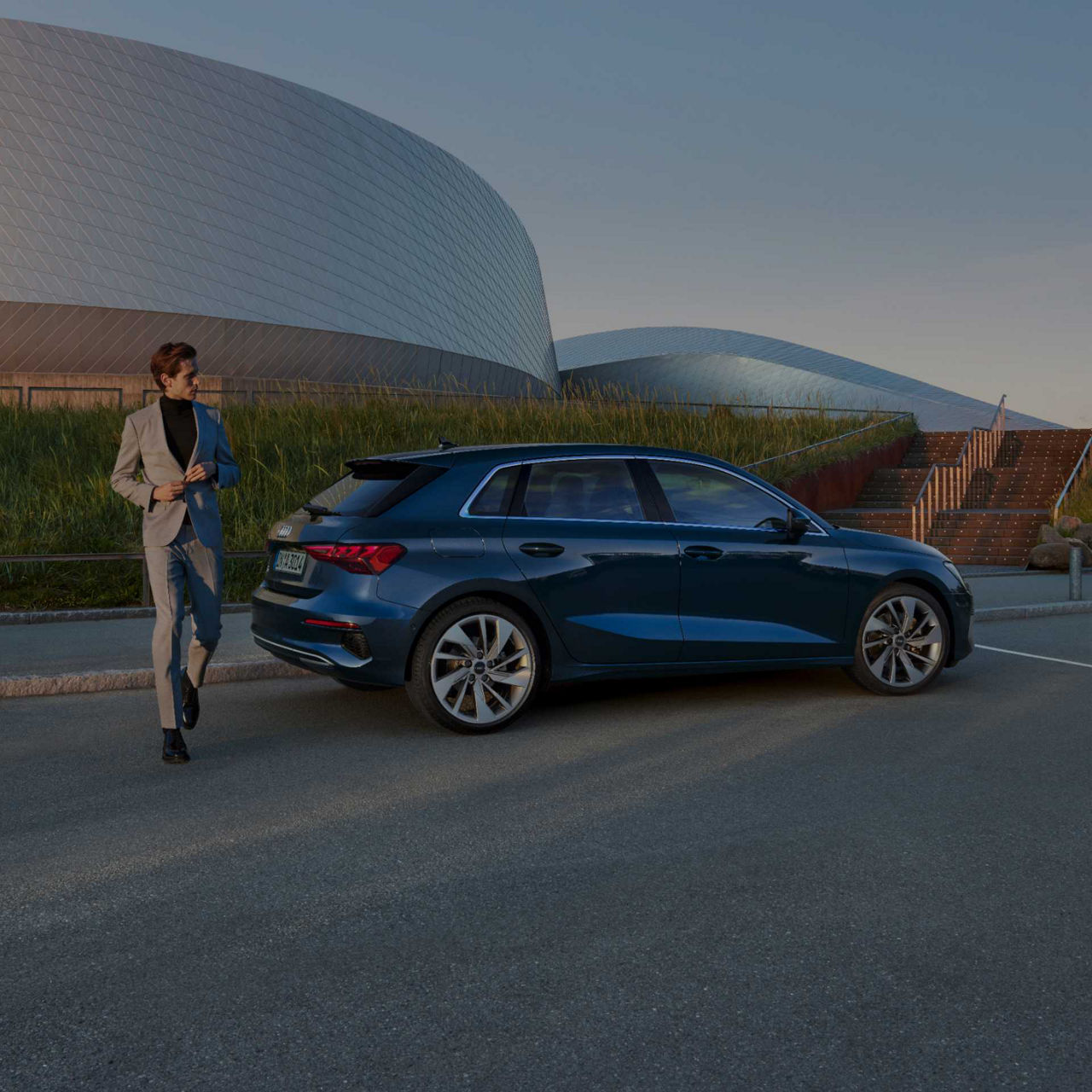 Man walking towards a modern building beside a parked blue Audi A3 Sportback car.