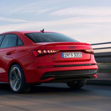 Red Audi sedan driving on a road, angled rear view in motion blur.