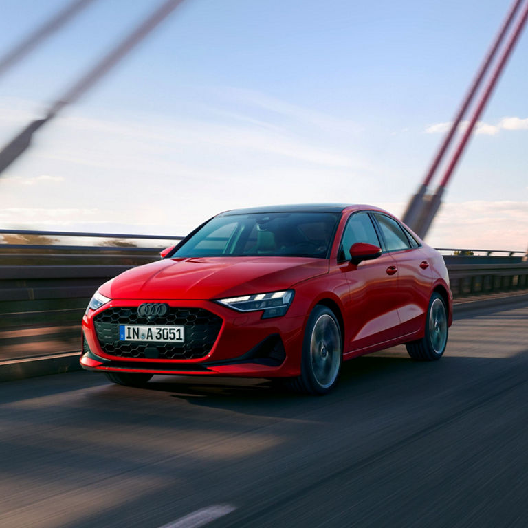 A red Audi car driving over a bridge, motion blur indicating speed.