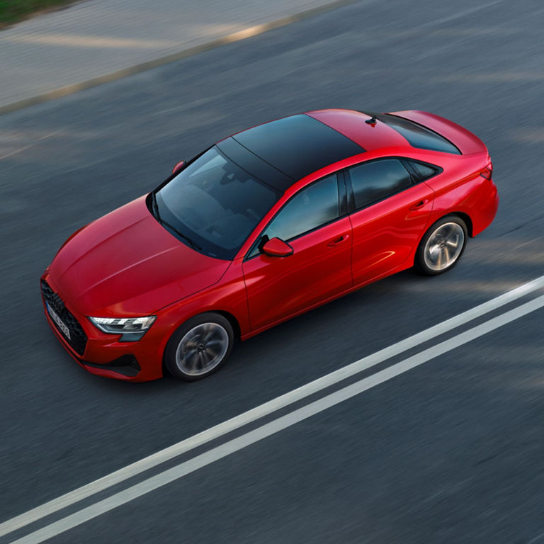 A red sedan driving on a road with visible lane markings, shot from a high angle.