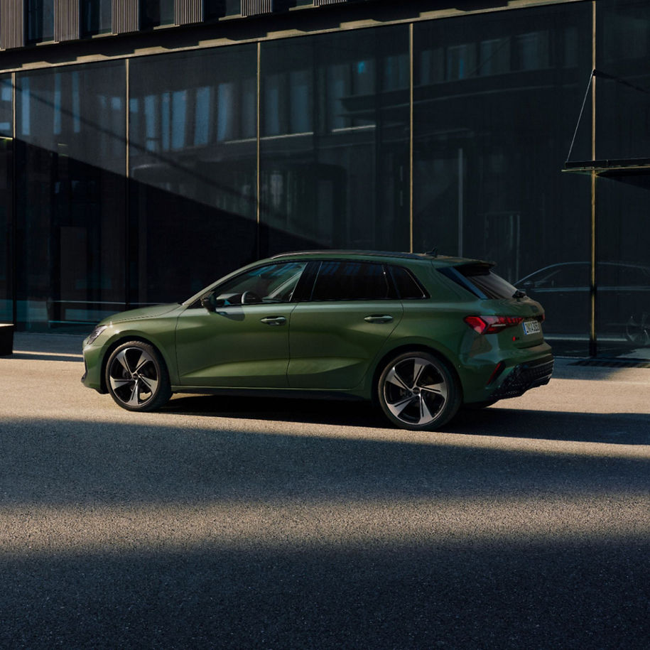 A green Audi A3 Sportback car parked on a city street with glass buildings in the background.