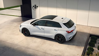 White hatchback car parked outside modern house near wall-mounted charging unit.