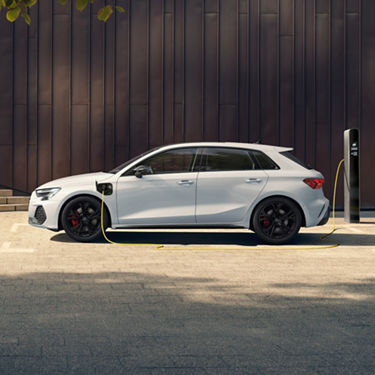 White electric car charging at a public charging station with a modern dark facade in the background.