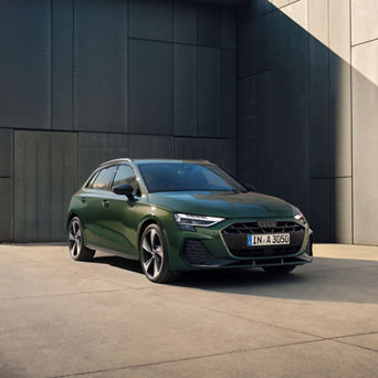 Green Audi A3 Sportback parked in front of a dark wall with sunlight casting a shadow on the right side.