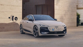 An Audi electric vehicle is parked next to a wall-mounted charger outside a modern building.